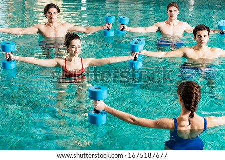 Trainer holding barbells while exercising with group of young people in swimming pool Royalty-Free Stock Photo #1675187677