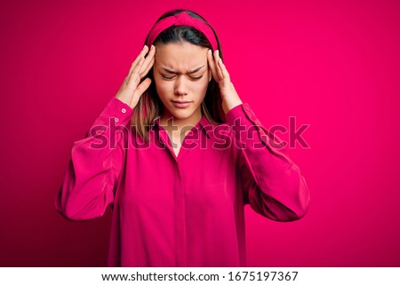 Young beautiful brunette girl wearing casual shirt standing over isolated pink background with hand on head for pain in head because stress. Suffering migraine.