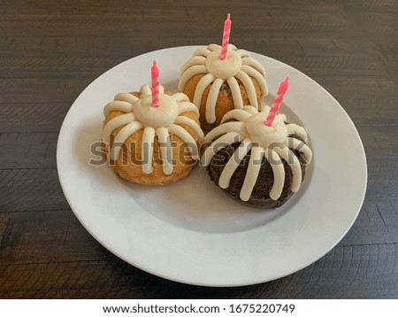 Three mini bundt cakes with frosting and pink birthday candles. 