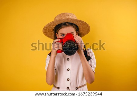 Young girl holding a camera in her hands on a yellow background and taking pictures