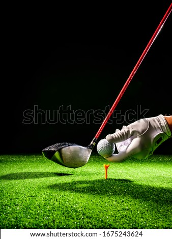 Golf ball positioned on the tee of a golf course with a golf driver on the wet course