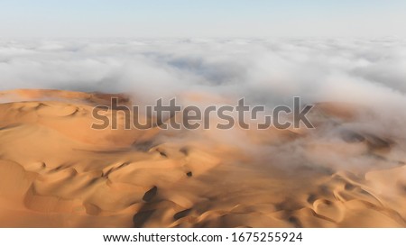 Aerial view of a massive sand dune surrounded by winter morning fog cloud in Empty Quarter. Liwa desert, Abu Dhabi, United Arab Emirates. Royalty-Free Stock Photo #1675255924