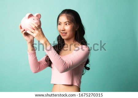 Young Asian woman with a pig coin bank on cyan background