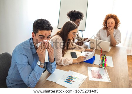 Cropped shot of a businessman suffering with allergies in an office. Shot of a frustrated businessman using a tissue to sneeze in while being seated in the office. Working when sick