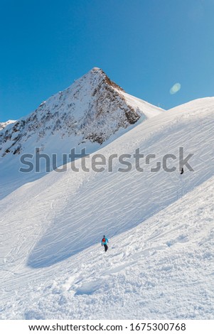 Beautiful snowy mountain panorama, clear blue ski background, few unrecognizable riders and ski lines on it. Vertical picture with back light. Actual extreme hobby and lifestyle.