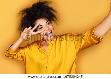 Cheerful girl taking selfie on the phone. Photo of african american girl on yellow background