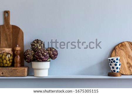 Modern composition on the kitchen interior with vegetables, herbs, cutting board, cup of coffee, kitchen accessories and copy space on the shelf.