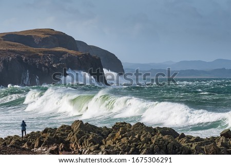 Photographer taking picture of large waves coming in from the Atlantic ocean on the rocky shore at Dunaff County Donegal Ireland