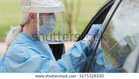 As part of the operations of a coronavirus mobile testing unit a healthcare worker dressed in full protective gear swabs an unseen person sitting inside of a vehicle.

 Royalty-Free Stock Photo #1675328320