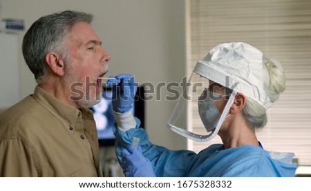 A mature Caucasian man in a clinical setting being swabbed by a healthcare worker in protective garb to determine if he has contracted the coronavirus or COVID-19. Royalty-Free Stock Photo #1675328332