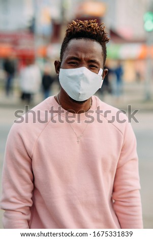 Portrait of young African man with a medical protective mask on his face at city street. Concept of preventive measures and protection for coronavirus pandemic.