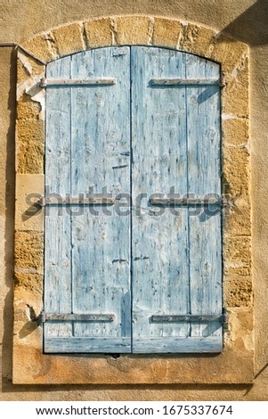 Vertical picture of typical traditional blue closed window shutters on stone yellow wall in Provence in sunny day. The facade of house in Lourmarin, one of the most beautiful villages of France.