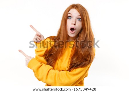 Shocked young redhead woman girl in casual yellow hoodie posing isolated on white background studio portrait. People emotions lifestyle concept. Mock up copy space. Pointing index fingers aside up