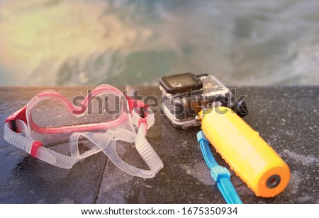 action camera with waterproof case and float stick and Googles on poolside of swimming pool on water background in summer beach holiday concept