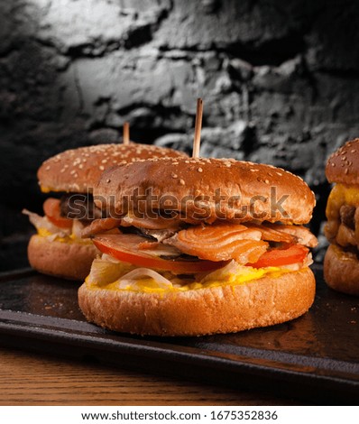 Menu of different burgers on one board. Side view of a fish burger, hamburger and cheese burger, against a wall background.