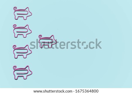 top view of pink piggy paper clips in one direction with leader isolated on blue, leadership concept