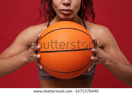 Cropped image of young african american sports fitness basketball player woman in sportswear working out isolated on red background in studio. Sport exercises healthy lifestyle concept. Holding ball
