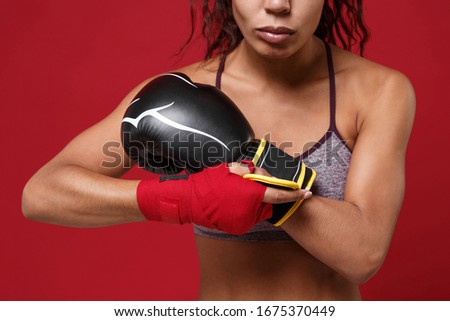 Cropped image of african american fitness boxer woman in sportswear working out isolated on red background. Sport exercise healthy lifestyle concept. Wearing sports bandages, putting on boxing gloves
