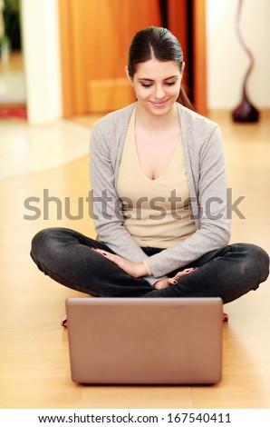 Young beautiful woman sitting on the floor and looking at it at home