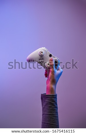 Hand with white gamepad on violet background. Gamer concept.