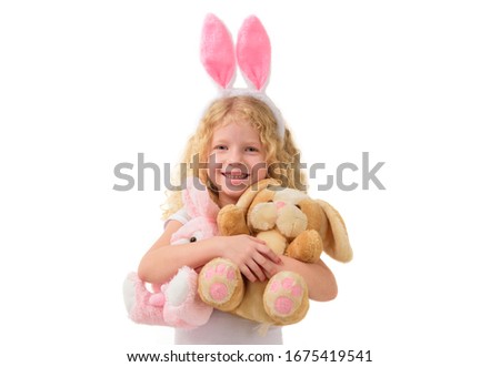 Cute little girl in the Easter bunny ears hugs two stuffed bunnies, isolated white background. The child smiles. Copy space.