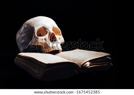 A human skull in the dark with a book clenched between its teeth. The concept of wisdom , reading, and the antiquity of science.