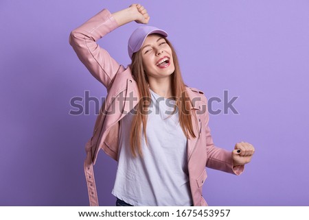 Picture of emotional cheerful energetic young female raising her arms, dancing, having fun, spending free time alone, being in high spirits, wearing casual clothes. People and emotions concept.