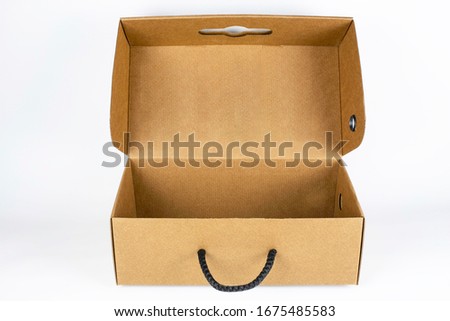 Open cardboard box with black handle on light background. The box is intended for packaging of shoes, clothes. Top view