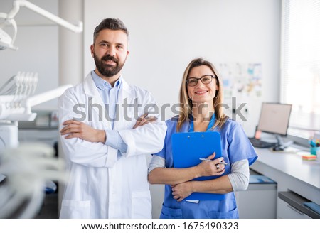 Dentist with dental assistant in modern dental surgery, looking at camera. Royalty-Free Stock Photo #1675490323