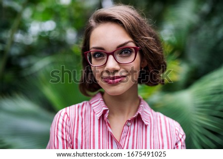 Young woman standing in botanical garden, looking at camera.