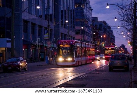 A streetcar on King street in Old Toronto district with cars, traffic lights, and street cars tracks glimmering in the darkness.