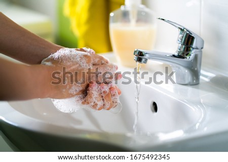 Caucasian woman washing her hands with soap in a white sink with silver faucet from which the water flows in the bright light. Preventive measures against Covid-19 (SARS-CoV-2) with hygienic hand gel. Royalty-Free Stock Photo #1675492345