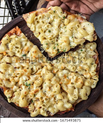 Macaroni and cheese pizza on wooden surface carried in hands
