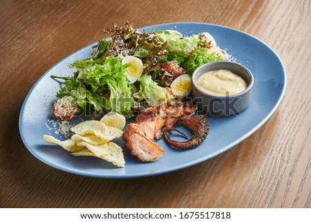 Caesar salad with croutons, parmesan, octopus, egg in whte bowl on white background. Restaurant serving. Close up with copy space.