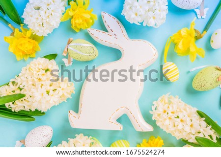 Easter scene with spring flowers, white rabbit and colored eggs, flat lay on blue background, toned