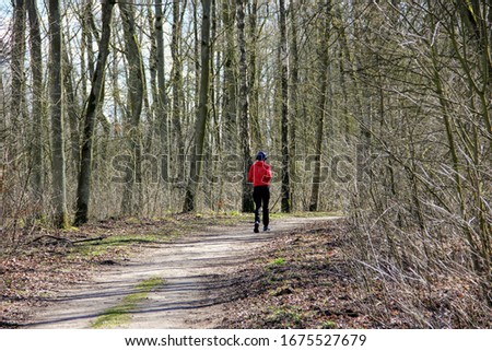 A man dressed in long sleeves runs with headphones on his ears along a path in the woods on a sunny spring day. (Photo from back)