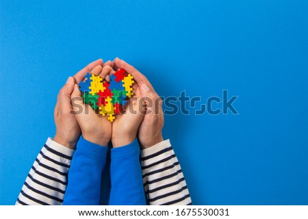 World autism awareness day concept. Adult and child hands holding puzzle heart on light blue background Royalty-Free Stock Photo #1675530031