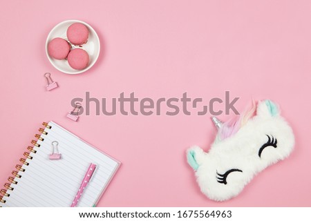 Modern female working space, top view. Cute women's or girls things, slleep mask, macarons, notepad, pen, clamps on pink backround, copy space, flat lay. Work from home concept. For blog. Horizontal. Royalty-Free Stock Photo #1675564963
