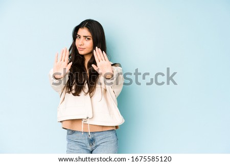 Young indian woman on blue background standing with outstretched hand showing stop sign, preventing you.