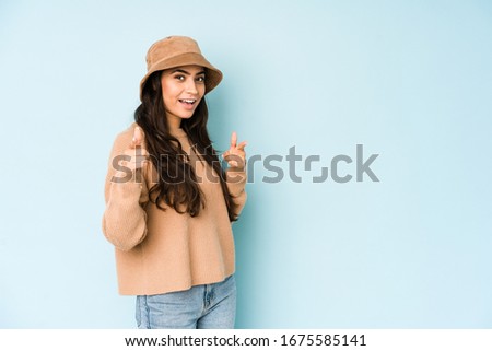Young indian woman wearing a hat isolated on blue background pointing to front with fingers.