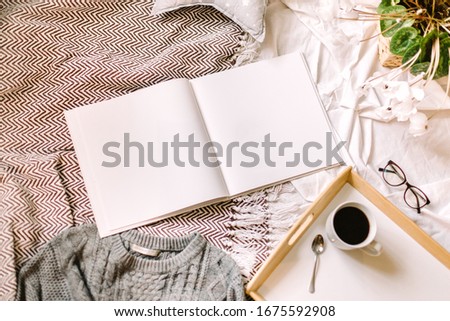 White book mockup. Square empty book. Album with clean pages on the bed with pillow, sweather and coffee. Clean book cover mockup. Flat Lay with mockup of the book. Lifestyle picture with white album.