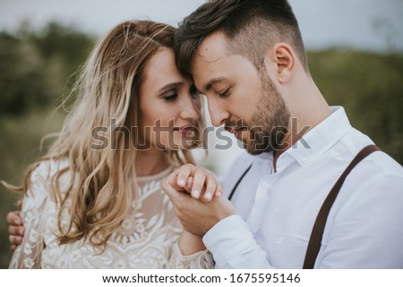 Smiling bride and groom spending time together. Posing on the mountain hills background. Dressed in white dress beautiful blonde caucasian bride and handsome groom.  