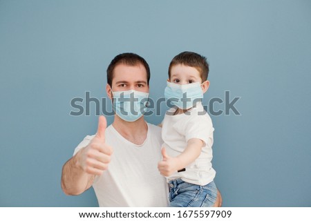 young father and his toddler son wearing surgical masks giving thumbs up to protection during the quarantine on a blue background Royalty-Free Stock Photo #1675597909