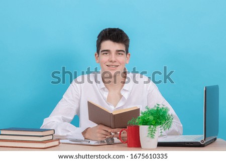 young male student at desk with book and computer studying