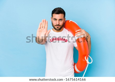 Young handsome lifeguard man isoalted standing with outstretched hand showing stop sign, preventing you.