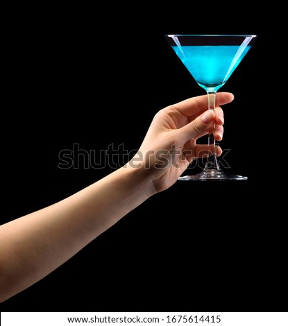 Woman hand holding blue martini glass isolated on black background with clipping path