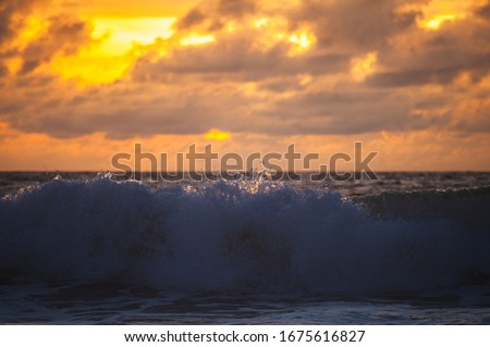 Magical dramatic sunset on a tropical beach. Seascape, ocean waves and bright clouds in the sky. Golden hour. Rest on the seashore, beach vacation. Concept.