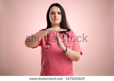 Portrait of beautiful woman doctor with stethoscope wearing pink scrubs, showing time out gesture posing on a pink isolated backround.