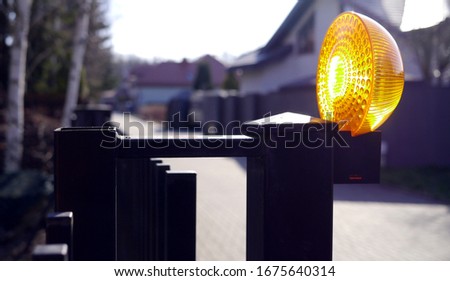 Entrance gate to the housing estate, residential buildings in the background, light warning about the gate opening. Guarded estate, entry only for residents. Entering the house.