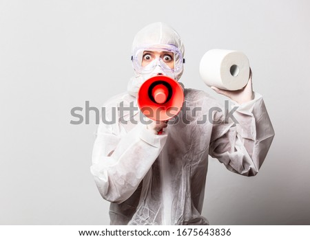 young doctor in protection suit and glasses with mask holds megaphone and toilet paper on white background